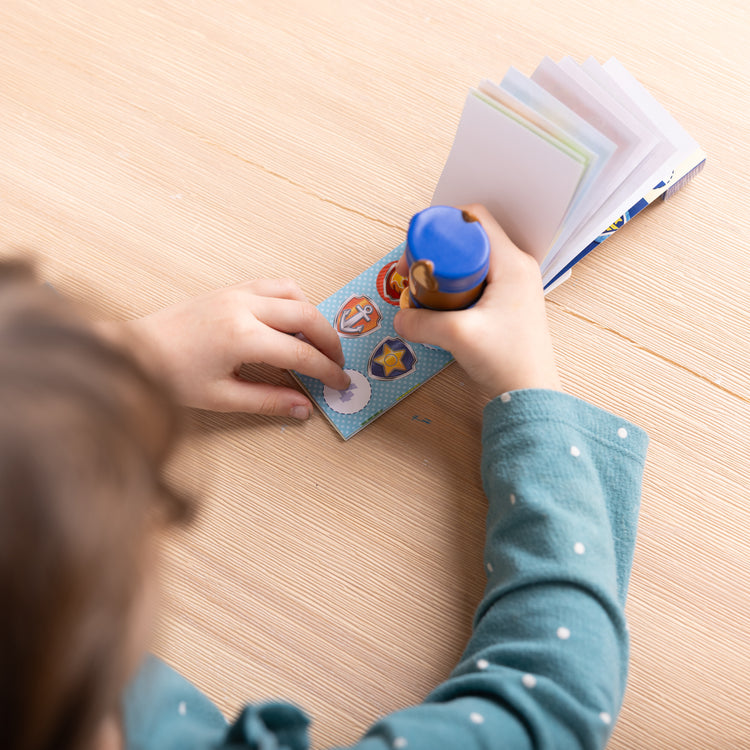 A kid playing with The Melissa & Doug Sticker WOW!™ Mini Activity Pad and 200+ Refill Stickers for Sticker Stamper Arts and Crafts Fidget Toy Collectibles – PAW Patrol Stickers