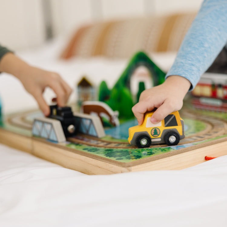 A kid playing with The Melissa & Doug 17-Piece Wooden Take-Along Tabletop Railroad, 3 Trains, Truck, Play Pieces, Bridge
