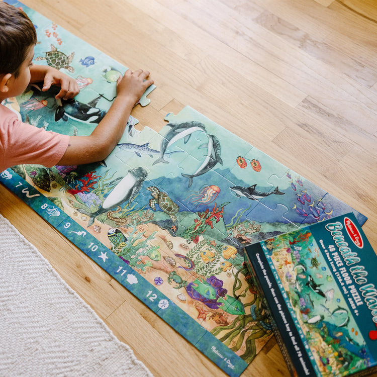 A kid playing with The Melissa & Doug Search and Find Beneath the Waves Floor Puzzle (48 pcs, over 4 feet long)