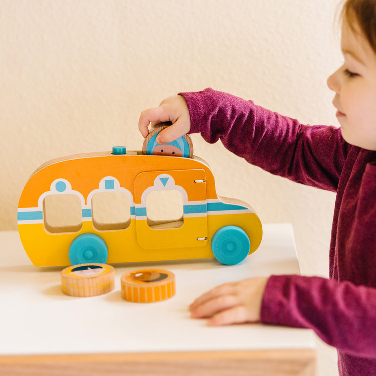 A kid playing with The Melissa & Doug GO Tots Wooden Roll & Ride Bus with 3 Disks