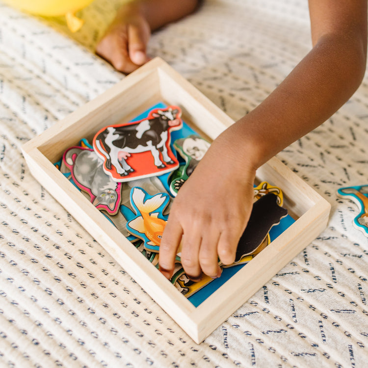 A kid playing with The Melissa & Doug 20 Wooden Animal Magnets in a Box