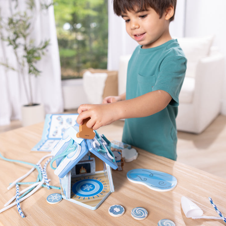 A kid playing with The Melissa & Doug Winter Frost Wooden Gingerbread House Play Set for Boys and Girls 3+ 