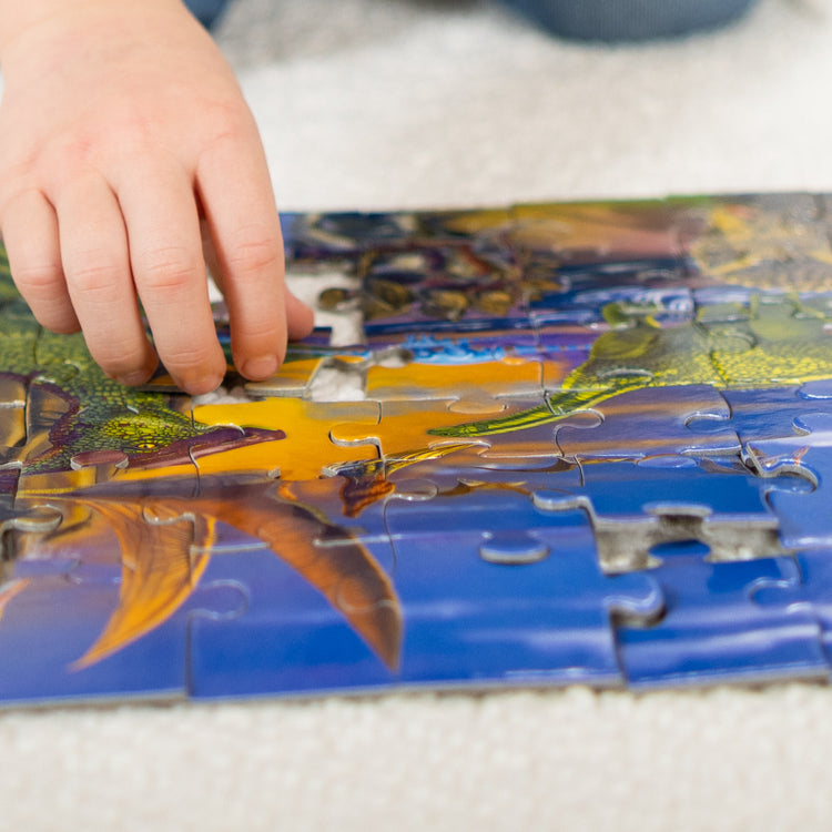 A kid playing with The Melissa & Doug Land of Dinosaurs Jigsaw Puzzle (60 pcs)