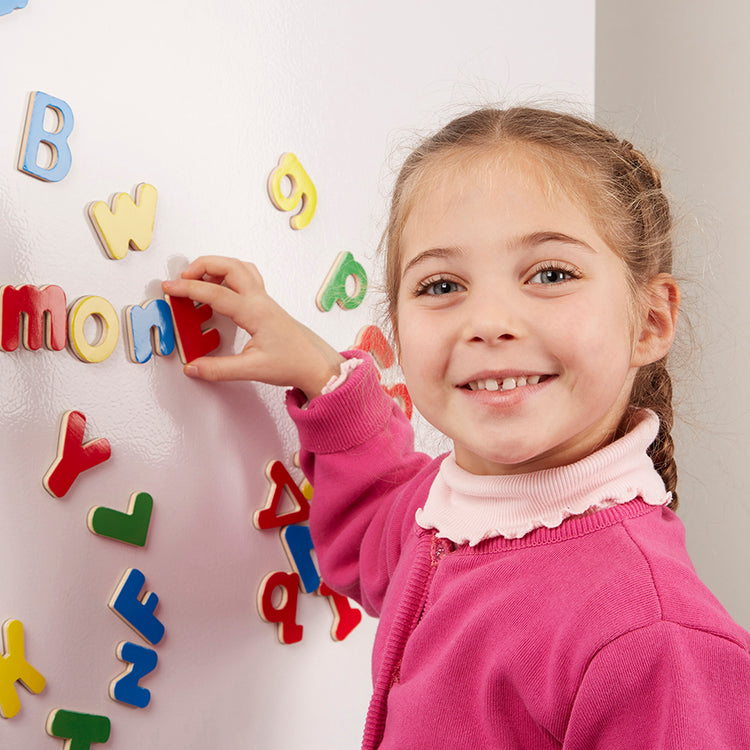 A kid playing with The Melissa & Doug 52 Wooden Alphabet Magnets in a Box - Uppercase and Lowercase Letters