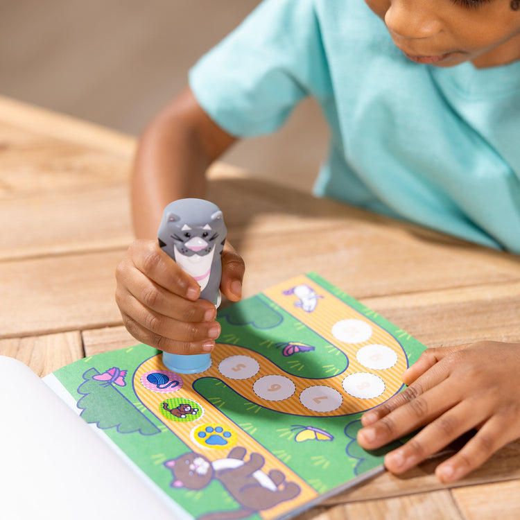 A kid playing with The Melissa & Doug Sticker WOW!™ Cat Bundle: 24-Page Activity Pad, Sticker Stamper, 600 Stickers, Arts and Crafts Fidget Toy Collectible Character