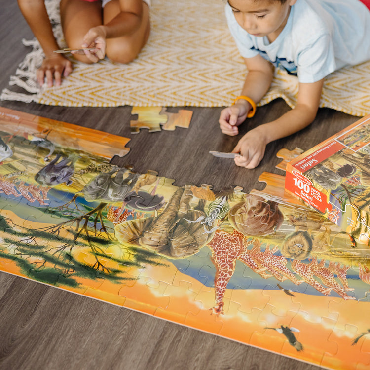 A kid playing with The Melissa & Doug African Plains Safari Jumbo Jigsaw Floor Puzzle (100 pcs, over 4 feet long)