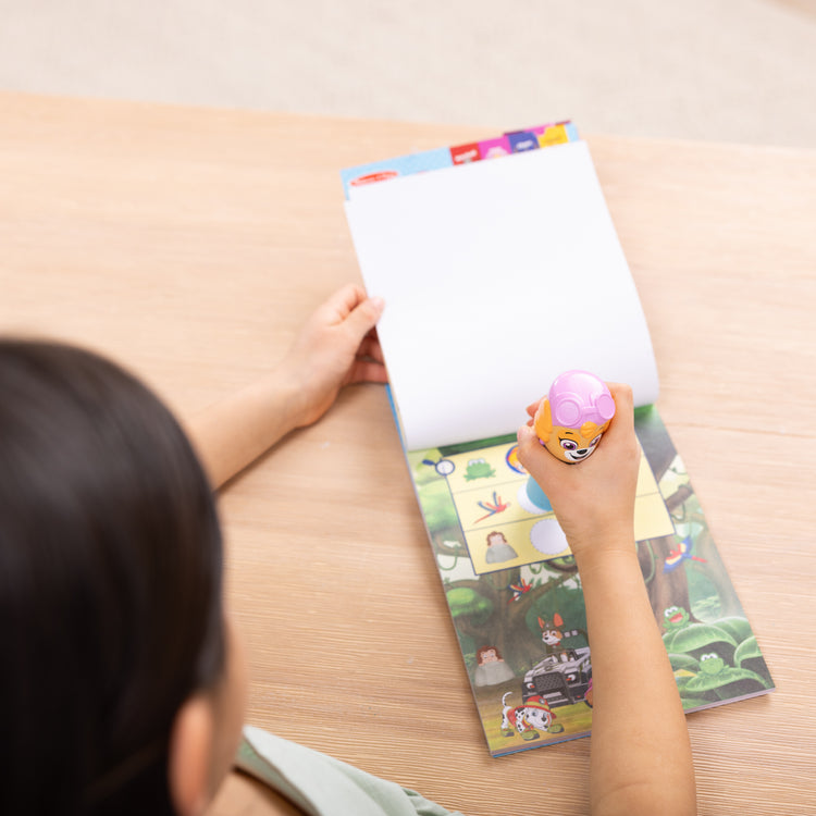 A kid playing with The Melissa & Doug Sticker WOW!™ PAW Patrol Skye Bundle: 24-Page Activity Pad, Sticker Stamper, 500 Stickers, Mini Pad, Arts and Crafts Fidget Toy Collectible Character