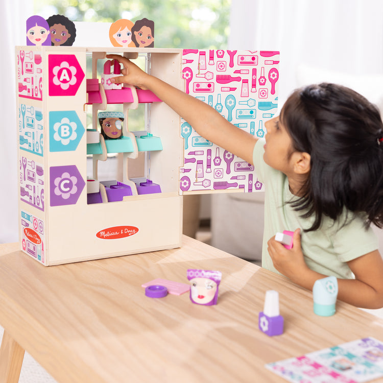 A kid playing with The Melissa & Doug Sort, Stock, Select Beauty Kiosk Vending Machine Play Set, Pretend Makeup Wooden Toy For Boys and For Girls 3+