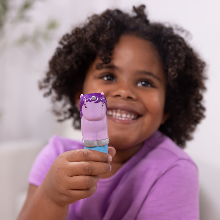 A kid playing with The Melissa & Doug Sticker WOW!™ 24-Page Activity Pad and Sticker Stamper, 300 Stickers, Arts and Crafts Fidget Toy Collectible Character – Sprinkles the Purple Unicorn