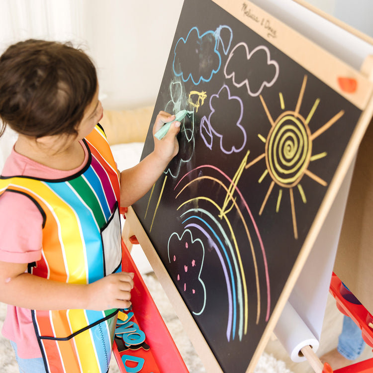 A kid playing with The Melissa & Doug Deluxe Magnetic Standing Art Easel With Chalkboard, Dry-Erase Board, and 39 Letter and Number Magnets