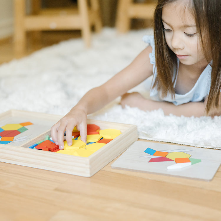 A kid playing with The Melissa & Doug Pattern Blocks and Boards - Classic Toy With 120 Solid Wood Shapes and 5 Double-Sided Panels, Multi-Colored Animals Puzzle
