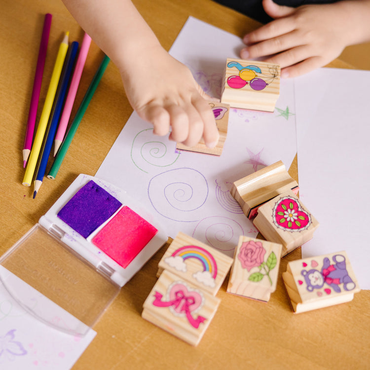 A kid playing with The Melissa & Doug Wooden Stamp Set: Friendship - 9 Stamps, 5 Colored Pencils, and 2-Color Stamp Pad