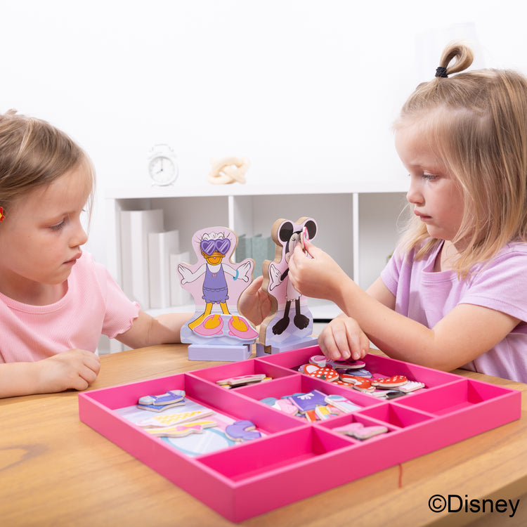 A kid playing with The Melissa & Doug Disney Minnie Mouse and Daisy Duck Deluxe Wooden Magnetic Dress-Up; 2 Fashion Dolls with Stands for Pretend Play, 52 Pieces