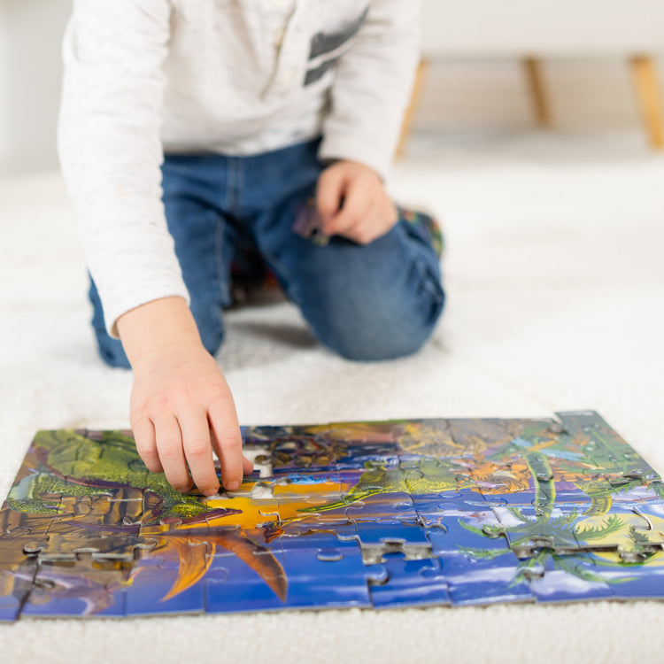 A kid playing with The Melissa & Doug Land of Dinosaurs Jigsaw Puzzle (60 pcs)