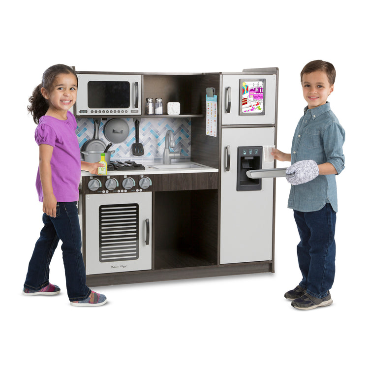 A child on white background with The Melissa & Doug Chef's Wooden Pretend Play Kitchen for Kids With “Ice” Cube Dispenser – Charcoal Gray