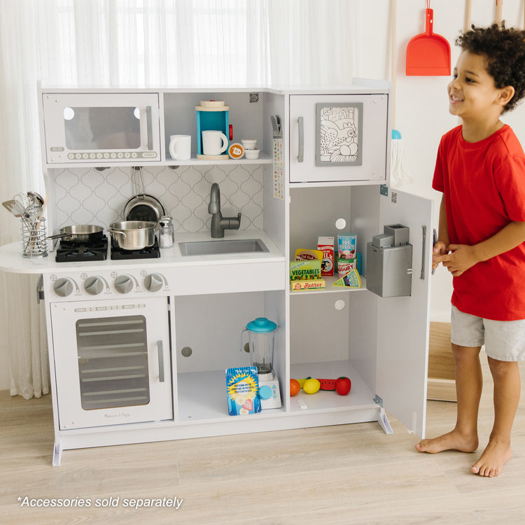 A kid playing with The Melissa & Doug Wooden Chef’s Pretend Play Toy Kitchen With “Ice” Cube Dispenser – Cloud White