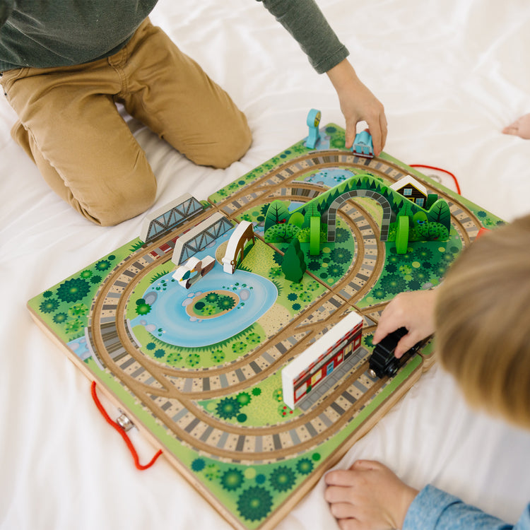 A kid playing with The Melissa & Doug 17-Piece Wooden Take-Along Tabletop Railroad, 3 Trains, Truck, Play Pieces, Bridge