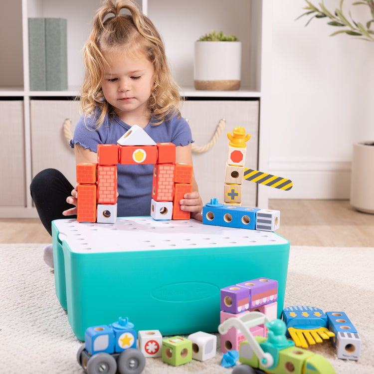 A kid playing with The Melissa & Doug Blockables™ Deluxe City Snap And Play Amazon Exclusive, Mix and Match Connectable Wooden Building Blocks Play Set With Storage Bin and Play Lid (122 Pcs)