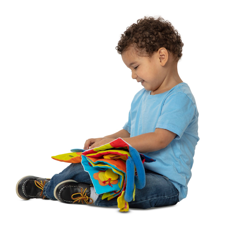 A child on white background with The Melissa & Doug K’s Kids My First Activity Book 8-Page Soft Book for Babies and Toddlers