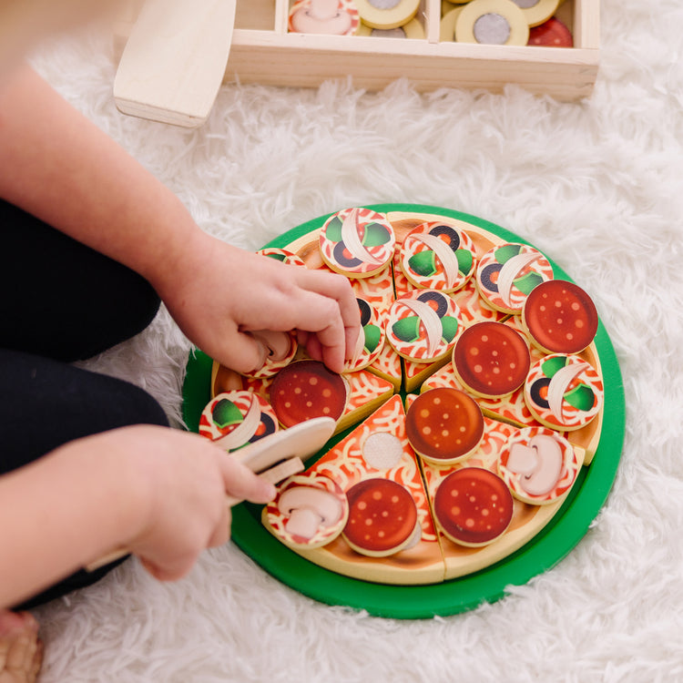 A kid playing with The Melissa & Doug Wooden Pizza Party Play Food Set With 36 Toppings