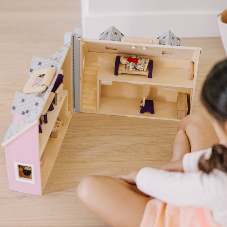 A kid playing with The Melissa & Doug Fold and Go Wooden Dollhouse With 2 Dolls and Wooden Furniture