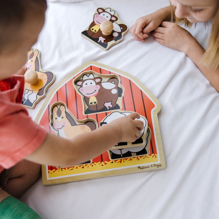 A kid playing with the Melissa & Doug Barnyard Animals Jumbo Knob Wooden Puzzle - Horse, Cow, and Sheep