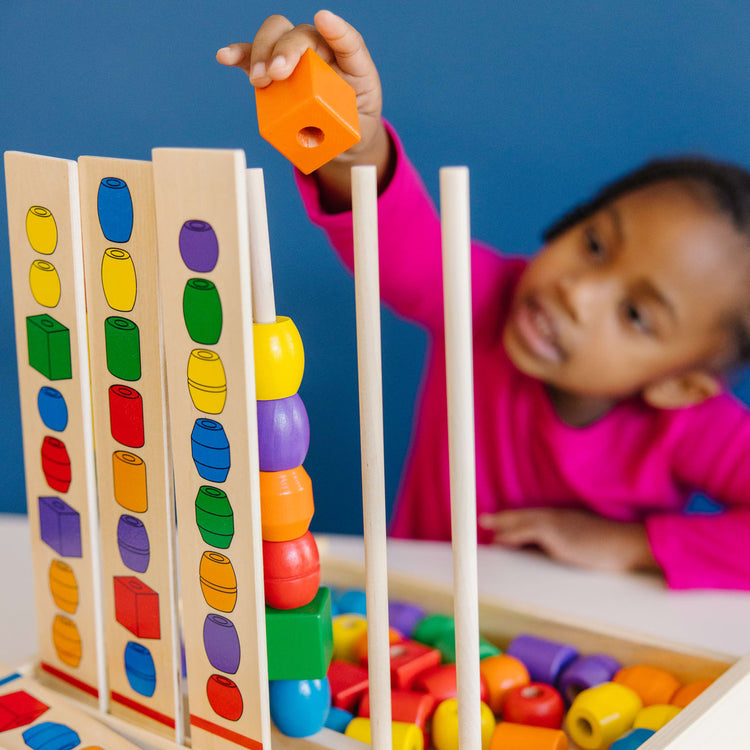 A kid playing with the Melissa & Doug Bead Sequencing Set With 46 Wooden Beads and 5 Double-Sided Pattern Boards