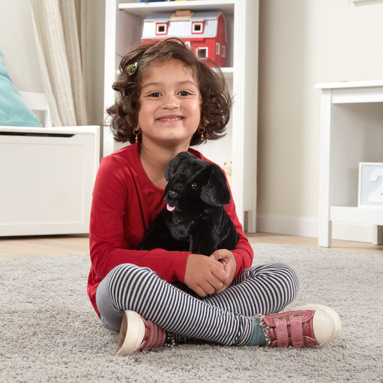 A kid playing with the Melissa & Doug Benson Black Lab - Stuffed Animal Puppy Dog