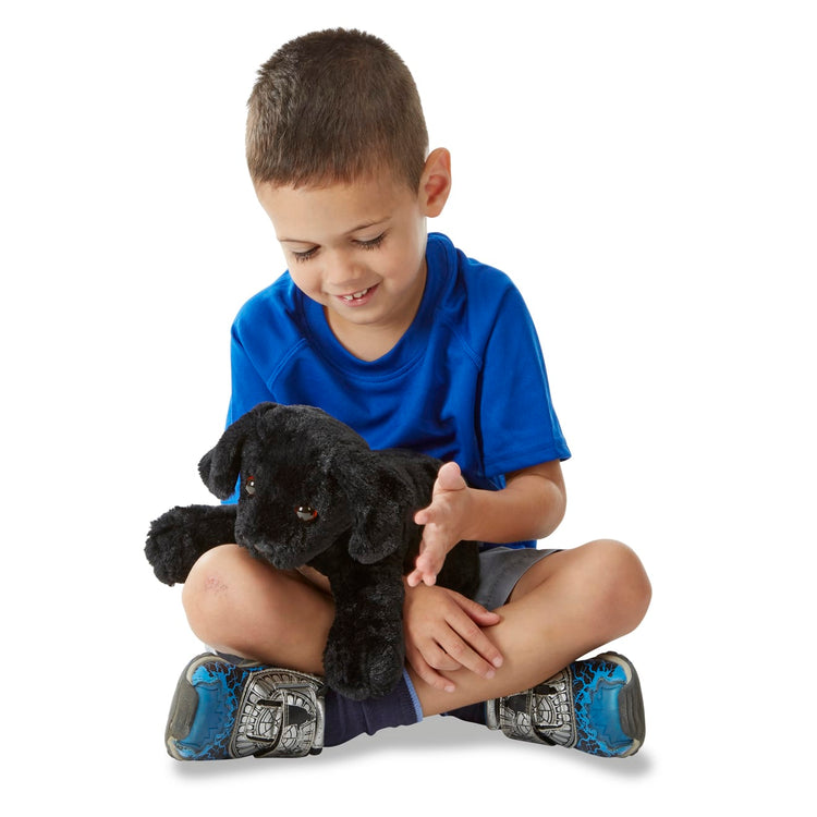 A child on white background with the Melissa & Doug Benson Black Lab - Stuffed Animal Puppy Dog