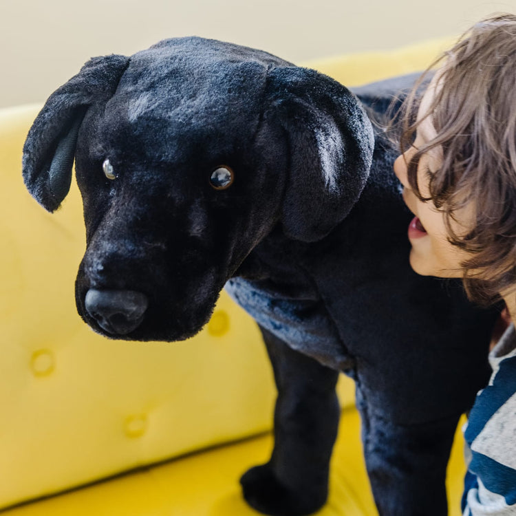 A kid playing with the Melissa & Doug Giant Black Lab - Lifelike Stuffed Animal Dog (over 2 feet tall)