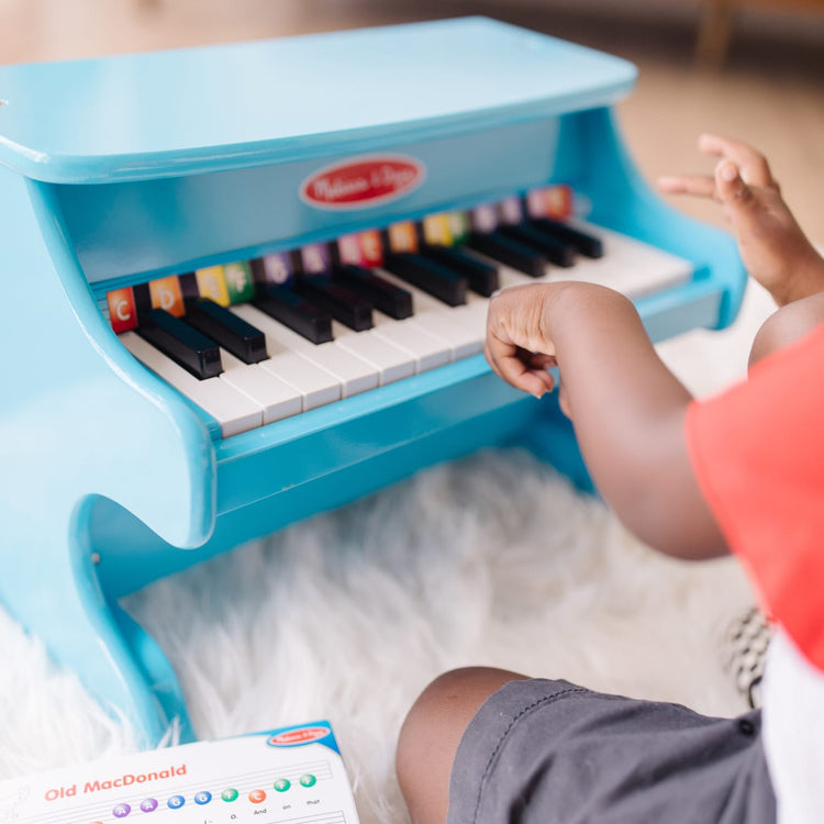 A kid playing with the Melissa & Doug Learn-to-Play Piano With 25 Keys and Color-Coded Songbook - Blue