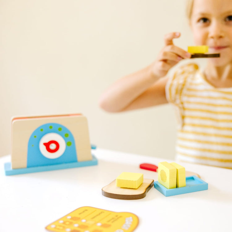 A kid playing with the Melissa & Doug Bread and Butter Toaster Set (9 pcs) - Wooden Play Food and Kitchen Accessories