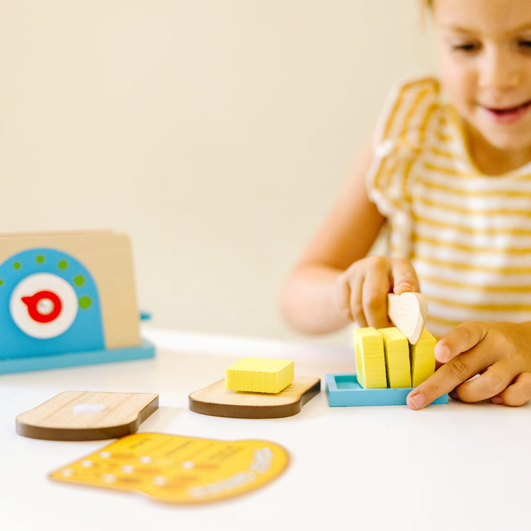 A kid playing with the Melissa & Doug Bread and Butter Toaster Set (9 pcs) - Wooden Play Food and Kitchen Accessories