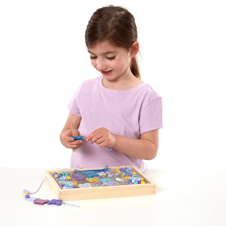 A child on white background with the Melissa & Doug Created by Me! Butterfly Beads Wooden Bead Kit, 150+ Beads for Jewelry-Making