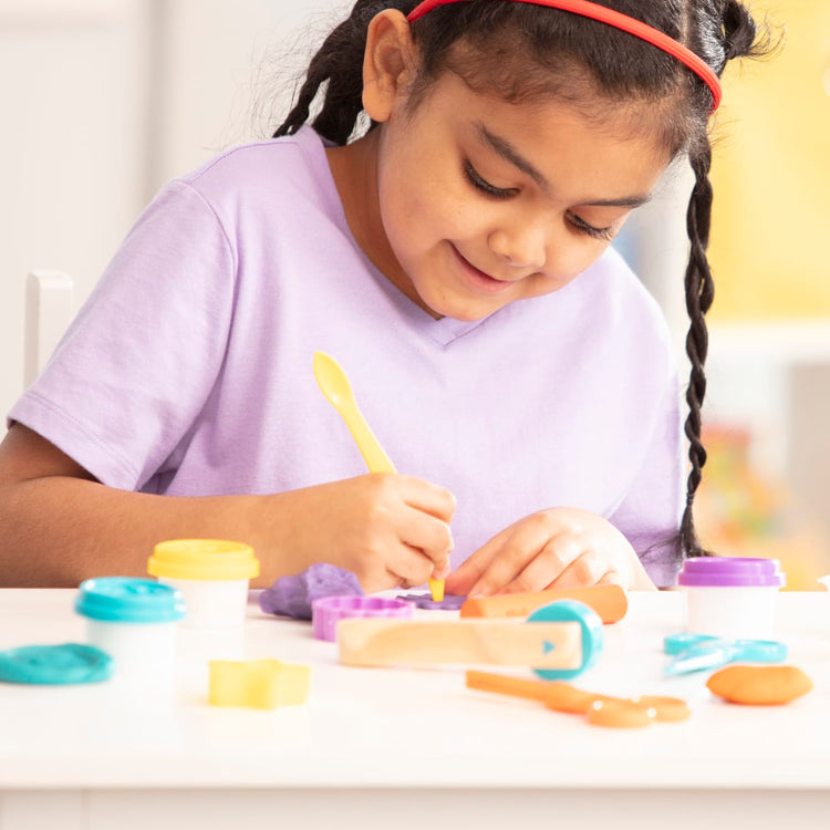 A kid playing with the Melissa & Doug Clay Play Activity Set - With Sculpting Tools and 8 Tubs of Modeling Dough