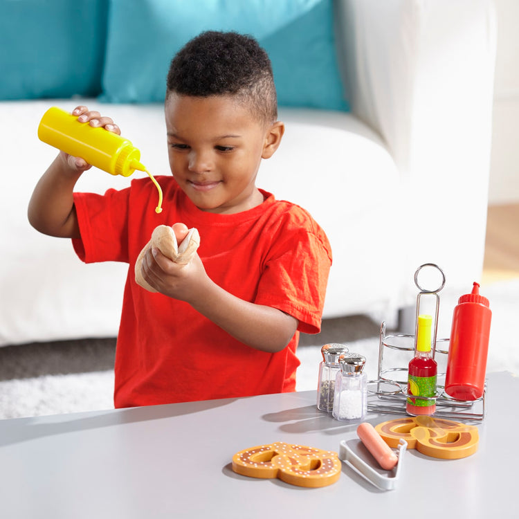 A kid playing with the Melissa & Doug Condiments Play Set (6 pcs) - Play Food, Stainless Steel Caddy