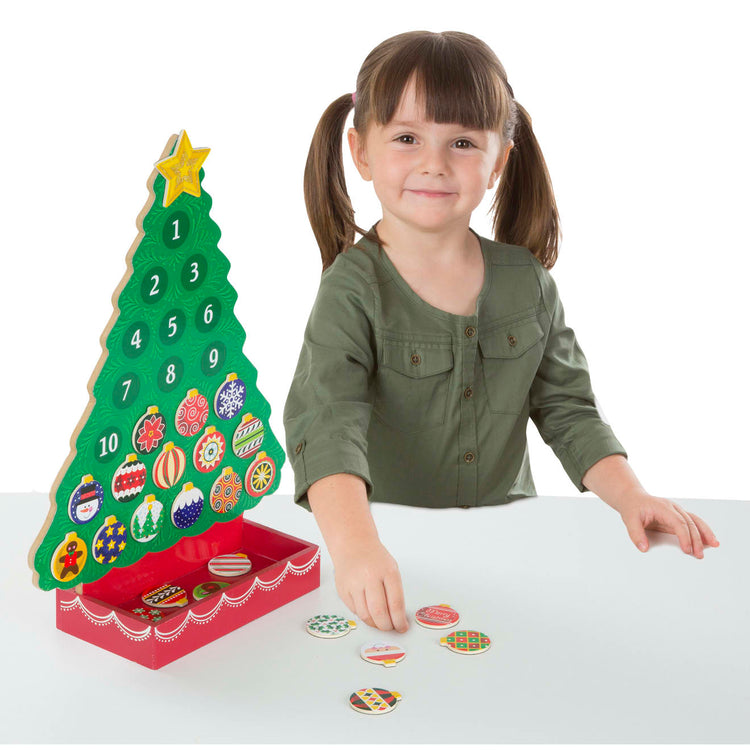 A child on white background with the Melissa & Doug Countdown to Christmas Wooden Advent Calendar - Magnetic Tree, 25 Magnets