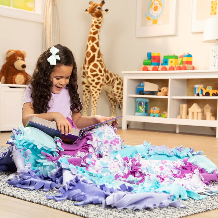 A kid playing with the Melissa & Doug Created by Me! Butterfly Fleece Quilt No-Sew Craft Kit (48 squares, 4 feet x 5 feet)
