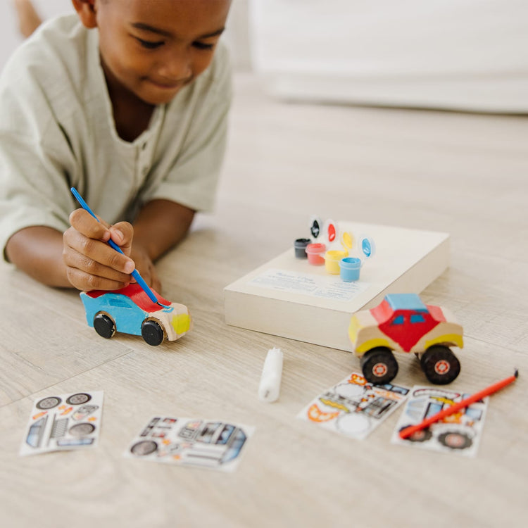 A kid playing with the Melissa & Doug Decorate-Your-Own Wooden Craft Kits Set - Race Car and Monster Truck
