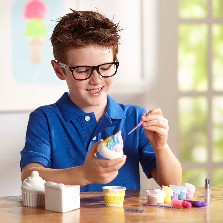 A kid playing with the Melissa & Doug Sweet Keepsakes Craft Kit: 2 Decorate-Your-Own Treasure Boxes and a Cake Bank