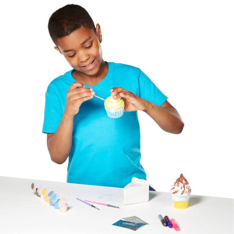 A child on white background with the Melissa & Doug Sweet Keepsakes Craft Kit: 2 Decorate-Your-Own Treasure Boxes and a Cake Bank