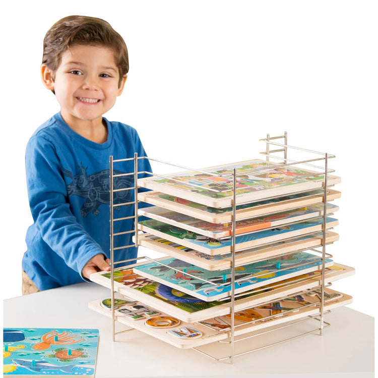 A child on white background with the Melissa & Doug Deluxe Metal Wire Puzzle Storage Rack for 12 Small and Large Puzzles