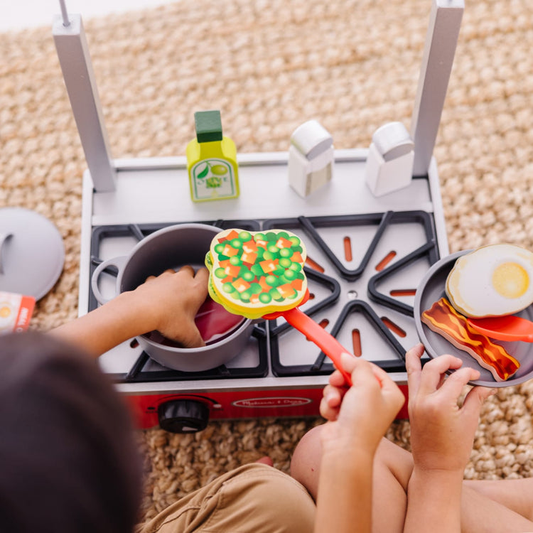 A kid playing with the Melissa & Doug 19-Piece Deluxe Wooden Cooktop Set With Wooden Play Food, Durable Pot and Pan