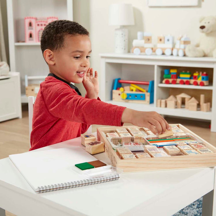 A kid playing with the Melissa & Doug Deluxe Wooden Stamp Set: Animals - 30 Stamps, 6 Markers, 2 Stamp Pads