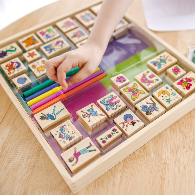A kid playing with the Melissa & Doug Deluxe Wooden Stamp and Coloring Set – Fairy Tale (30 Stamps, 6 Markers, 2 Durable 2-Color Stamp Pads)