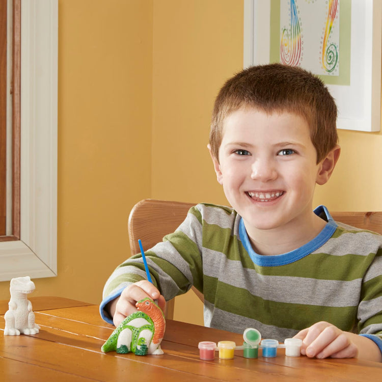 A kid playing with the Melissa & Doug Created by Me! Dinosaur Figurines Craft Kit (2 Resin Dinosaurs, 6 Paints, Paintbrush)