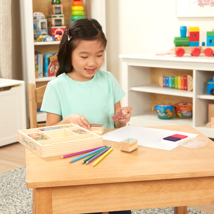 A kid playing with the Melissa & Doug Disney Princess Wooden Stamp Set: 9 Stamps, 5 Colored Pencils, and 2-Color Stamp Pad