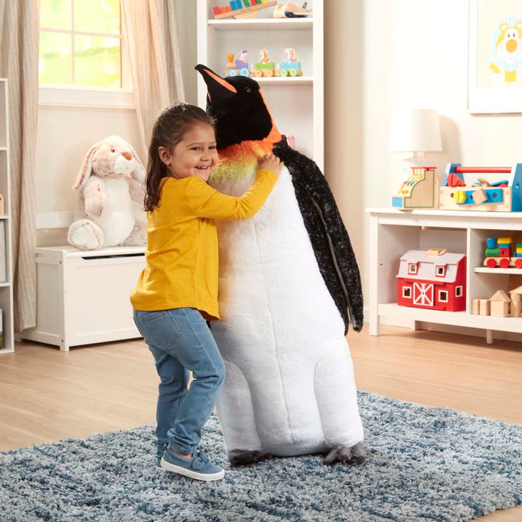 A kid playing with the Melissa & Doug Giant Lifelike Plush Emperor Penguin Standing Stuffed Animal (3.4 Feet Tall)