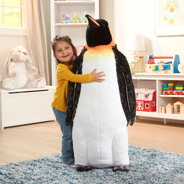 A kid playing with the Melissa & Doug Giant Lifelike Plush Emperor Penguin Standing Stuffed Animal (3.4 Feet Tall)