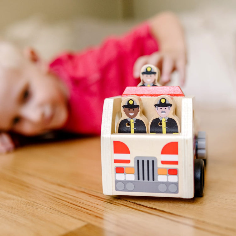 A kid playing with the Melissa & Doug Wooden Fire Truck With 3 Firefighter Play Figures